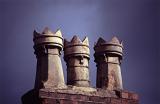 Row of chimney pots in Stockport on a rooftop, close up against a dark threatening stormy sky