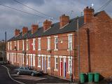 Red brick terraced houses with a Jaguar car parked in front and wheelie bins at the side