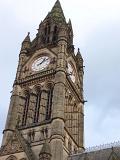Exterior ornate stone facade of the Gothic revival clock tower on Manchester Town Hall with its four clock faces, Lancashire, UK