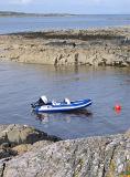 Rubber dinghy moored to a buoy in a coastal inlet between rock formations for fishing and water sport