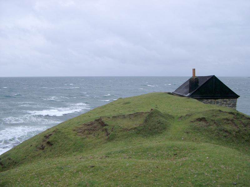 Seascape with the roof of a remote cottage or shed just visible above the headland overlooking a stormy sea on an overcast day