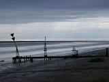Dark atmospheric landscape of a marine estuary on an overcast stormy day with a silhouette of a small jetty and warning signs on the beach in the foreground