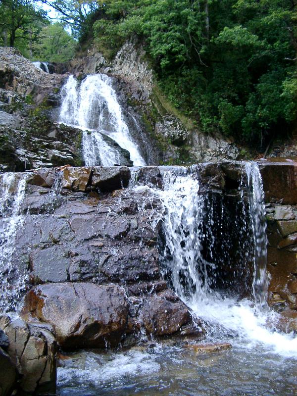 Rhaeadr Mawddach Falls, Wales, cascading down over layers of black rock in scenic lush green woodland vegetation