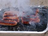 Sizzling Sausages Cooking on Outdoor Foil Pan Charcoal Grill