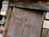 Closed up mine entrance with a wooden door and the warning - Keep out, danger deep well - painted on the exterior