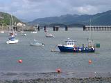 Fishing boats moored in the harbour at Barmouth with the viaduct carrying the railroad crossing the water in the background , Gwynedd, Wales