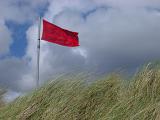 Looking Up at Red No Swimming Warning Flag on Windy Grassy Dune with Dark Clouds