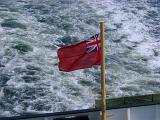 Red Scottish ensign flag flying off the stern of a ferry against the turbulence of the wake mid-ocean during a voyage