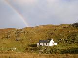 Picturesque whitewashed youth hostel in the Hebridies bathed in sunshine on a stormy day with grey clouds and a colorful rainbow