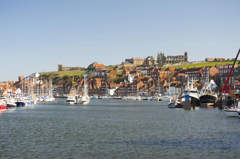 the river esk flowing through the coastal town of whitby with the landmark abbey standing on top of the hill