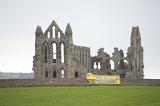 a yellow whitby tour bus drives past the abbey ruins