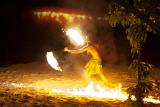 Fijian fire dancer performing on a beach amidst tongues of orange flames