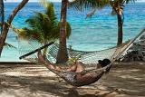 Man relaxing in a hammock strung between palm trees overlooking the ocean at a tropical island resort