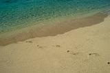 Empty tropical sandy beach with footprints leading from the sparkling clear blue sea diagonally across and then off frame
