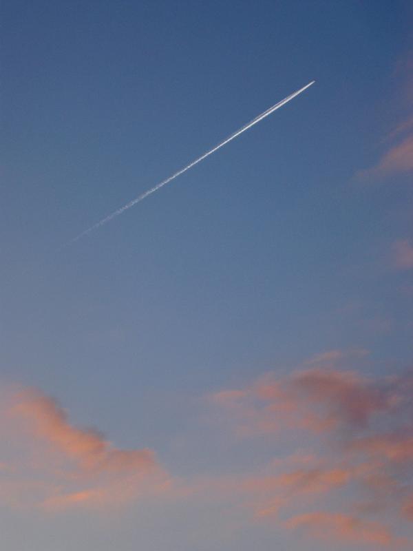 Jet trail or contrail in an evening sky with colorful pink clouds of condensed water vapor from a passing aircraft