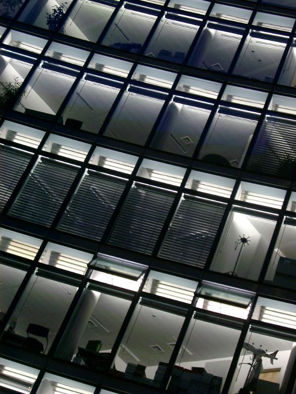 Rows of identical office windows in a high-rise building reflecting the surrounding urban environment, tilted angle of the exterior facade