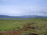 Remote path across the grassy lowland plains in Iceland with a meltwater lake and distant volcanic mountains