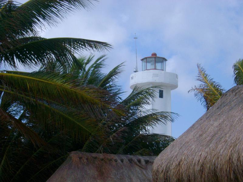 Lighthouse surrounded with palm trees viewed over the thatched roofs of beach cottages in Mexico