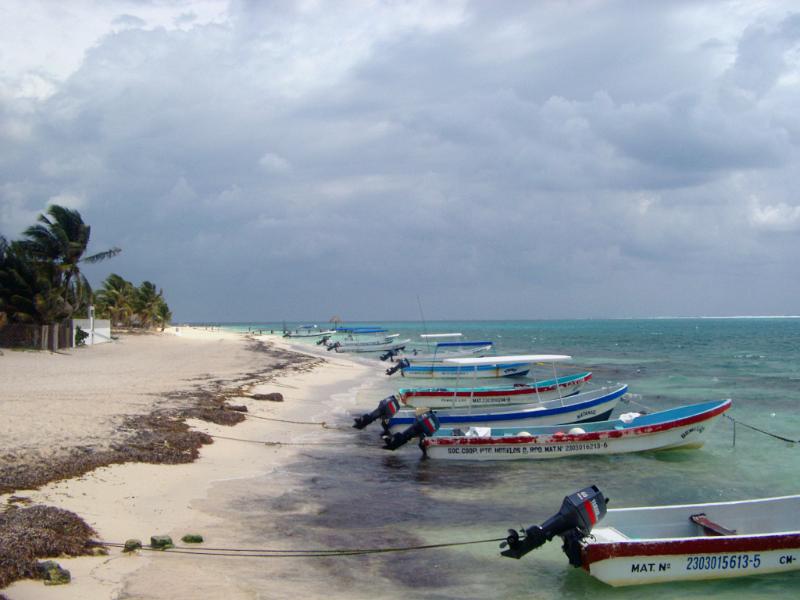 Small motorboats moored to the shoreline in Mexico with their bows pointing out to sea on a golden tropical beach under a cloudy summer sky