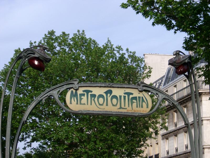 Art Deco Paris Metro sign with a typical swirling design and the word - Metropolitain - against urban buildings and trees