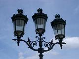 Paris lamppost with three lanterns in a typical Art Nouveau style of scrolling leaves against a cloudy blue sky