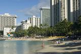 Random Tourists at Beautiful Seashore of Waikiki Beach. Captured with Huge Buildings at Beachfront.