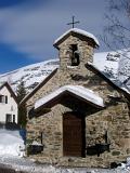 Snows on a Small Historic Alpine Christian Church During Winter Season. Captured with Light Blue Gray Sky Background.