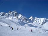 Random People Skiing on Winter Holiday Season with Huge Snow Covered Mountains View on Blue Gray Sky Background.