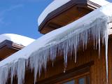 Icicles and a snow covered roof on a winter log holiday cabin against a clear blue sky in a vacation and travel concept